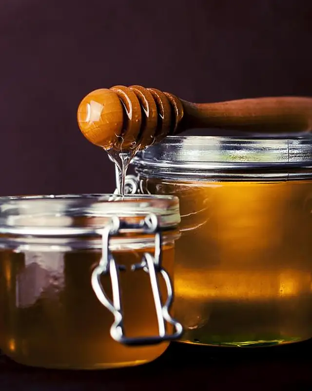 Jars of honey with a wooden dipper on a dark background.