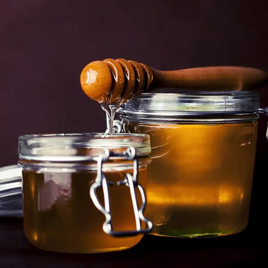Two glass jars of honey with a wooden honey dipper on a dark table.