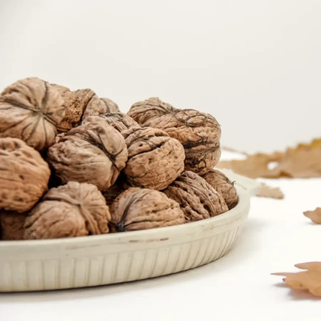 Walnuts in a shallow ceramic dish with dried leaves.